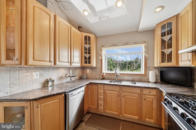 kitchen with stainless steel appliances, a sink, glass insert cabinets, backsplash, and dark stone countertops