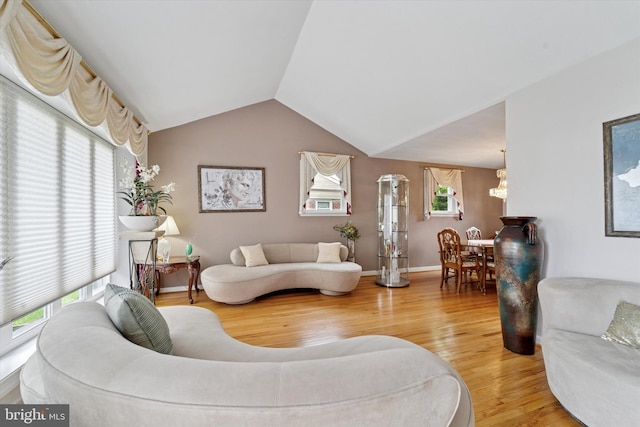 living area featuring wood finished floors, lofted ceiling, a chandelier, and baseboards