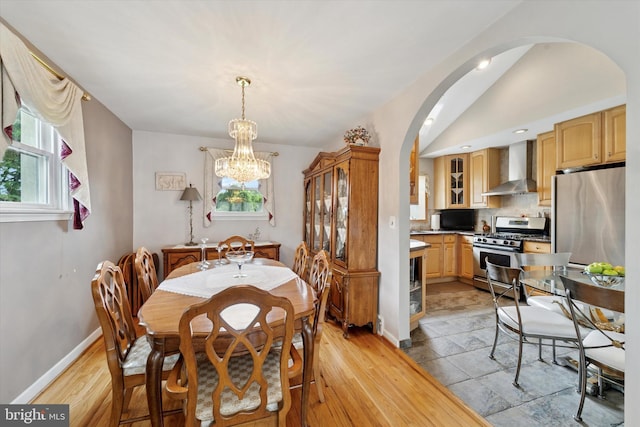 dining room with arched walkways, a chandelier, light wood-type flooring, and baseboards