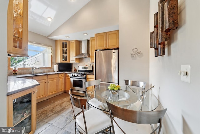 kitchen with appliances with stainless steel finishes, wall chimney exhaust hood, vaulted ceiling, backsplash, and a sink