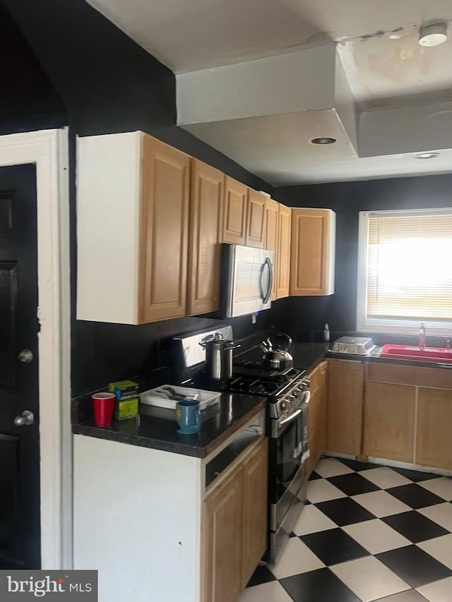 kitchen with stainless steel appliances, a sink, light brown cabinets, dark countertops, and light floors