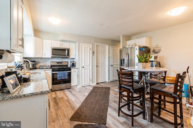 6402 Browning Rd, Pennsauken, NJ 08109 - kitchen featuring stainless steel appliances, white cabinets, a sink, light stone countertops, and light wood finished floors