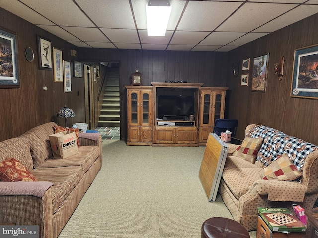 living area featuring stairs, a drop ceiling, light carpet, and wood walls