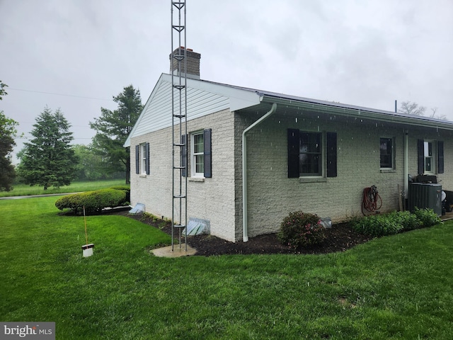 view of home's exterior with a chimney, a lawn, brick siding, and central AC unit
