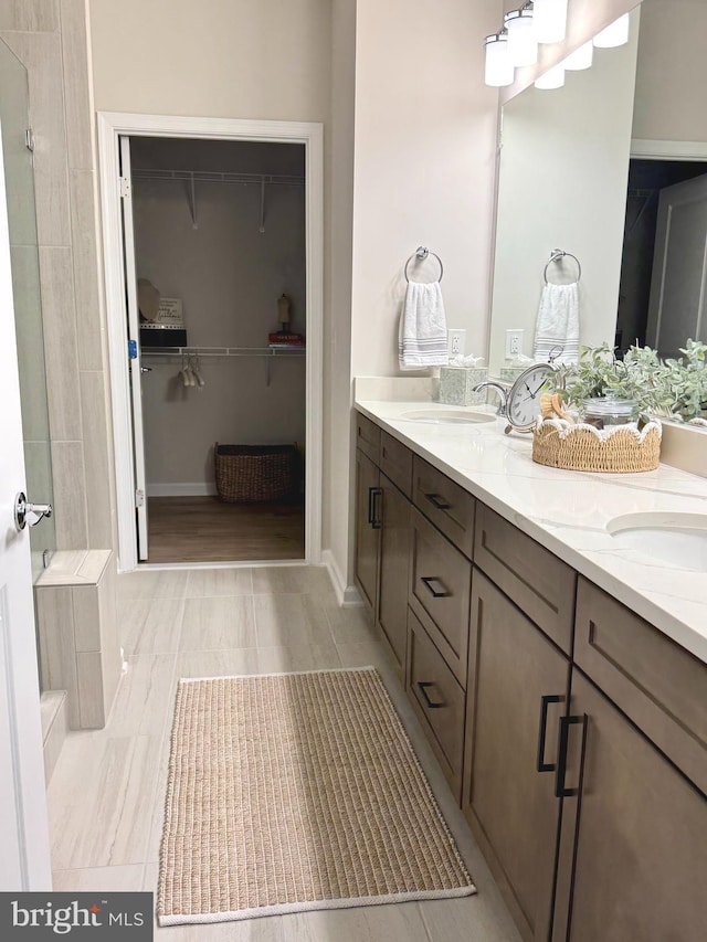 15741 Gardenia Ridge Way, Haymarket, VA 20169 - full bathroom with double vanity, a spacious closet, tiled shower, and baseboards