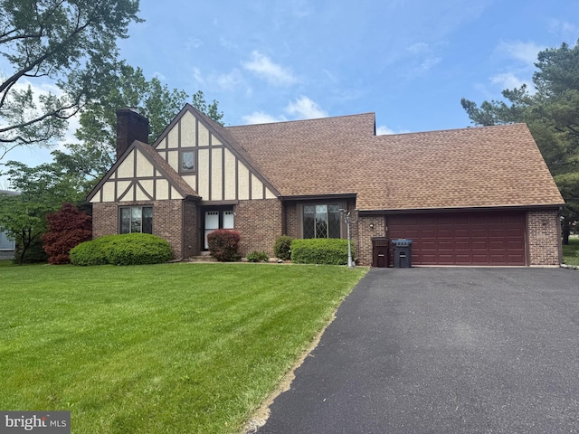 tudor home with brick siding, a front lawn, an attached garage, roof with shingles, and a chimney