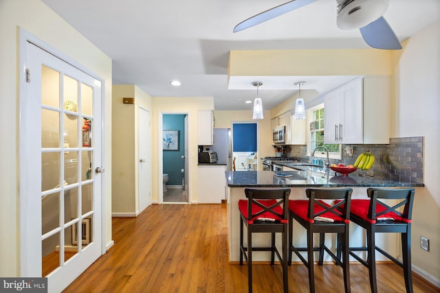 5455 Crowflock Ct, Columbia, MD 21045 - kitchen with appliances with stainless steel finishes, white cabinets, backsplash, a peninsula, and wood finished floors