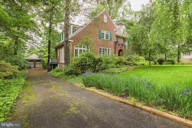 tudor-style house featuring brick siding, a garage, a front yard, and a chimney