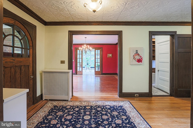 entryway with wood-type flooring, baseboards, a chandelier, an ornate ceiling, and crown molding