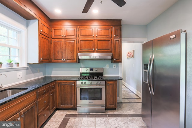 kitchen featuring appliances with stainless steel finishes, under cabinet range hood, a sink, ceiling fan, and dark stone counters