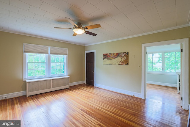 empty room featuring radiator heating unit, crown molding, plenty of natural light, ceiling fan, and hardwood / wood-style flooring