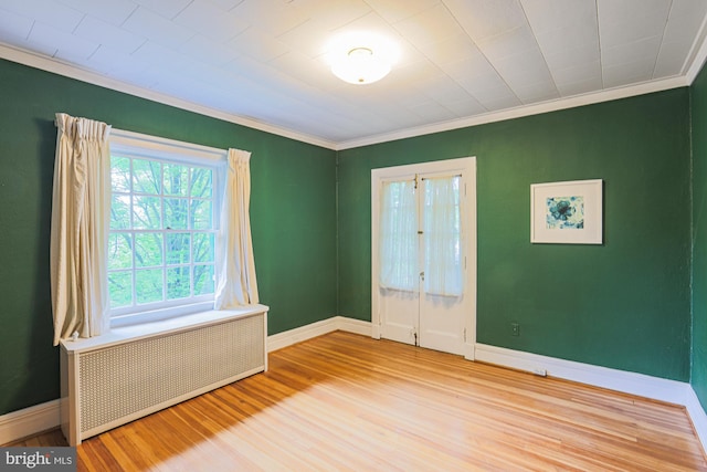 empty room with radiator, wood finished floors, ornamental molding, and baseboards