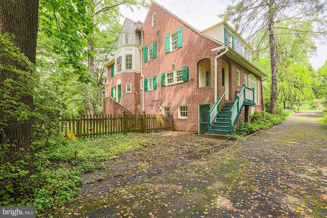 view of side of home with fence, brick siding, and stairway