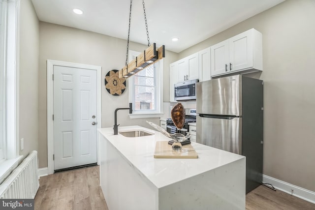 kitchen with stainless steel appliances, radiator heating unit, light wood-style floors, a sink, and recessed lighting