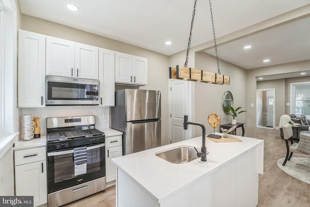 kitchen with appliances with stainless steel finishes, a sink, white cabinetry, light wood-style flooring, and light countertops