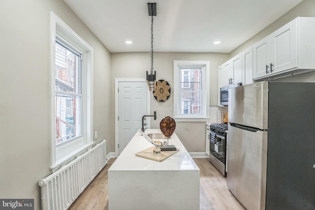 kitchen featuring appliances with stainless steel finishes, radiator, a sink, white cabinetry, and light wood-style floors
