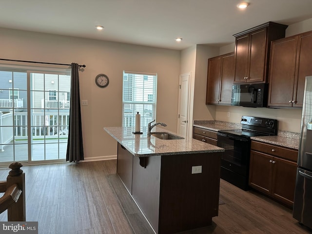 kitchen featuring black appliances, a sink, dark wood-type flooring, a kitchen island with sink, and light stone counters