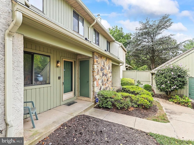 property entrance with board and batten siding, stone siding, and fence