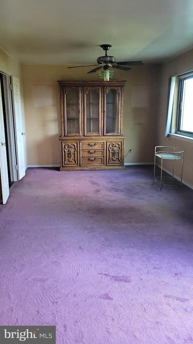carpeted spare room featuring ceiling fan and baseboards