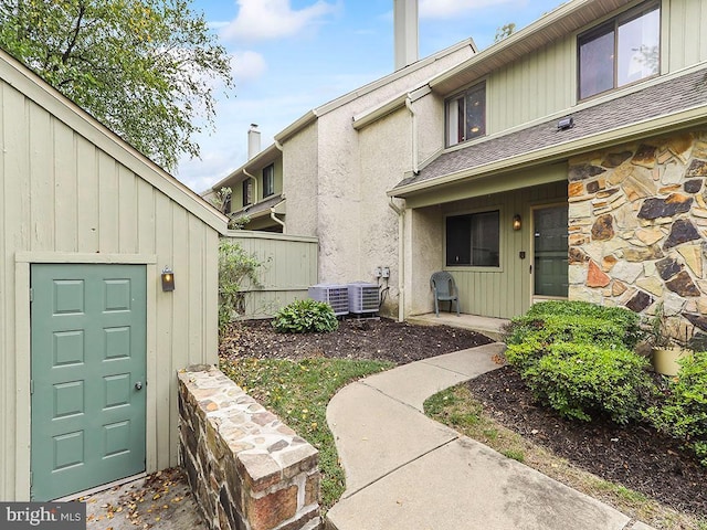 property entrance featuring central AC, fence, a chimney, and stone siding