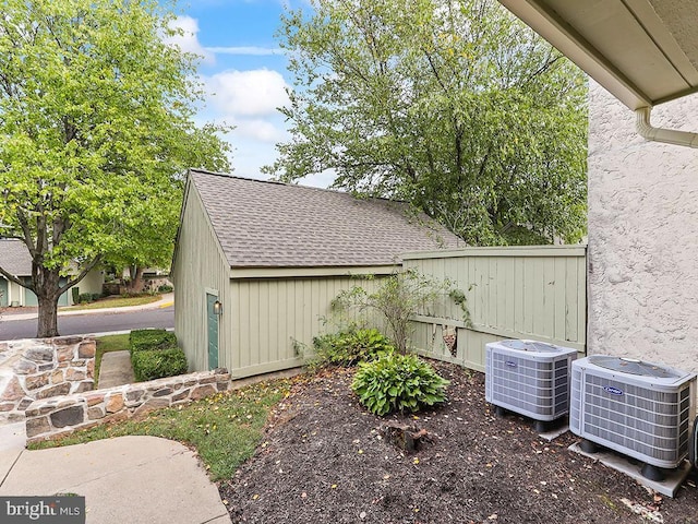 view of property exterior featuring central AC unit, a shingled roof, and fence