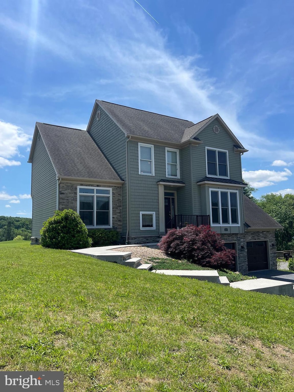 view of front of property with stone siding, a front lawn, driveway, and roof with shingles