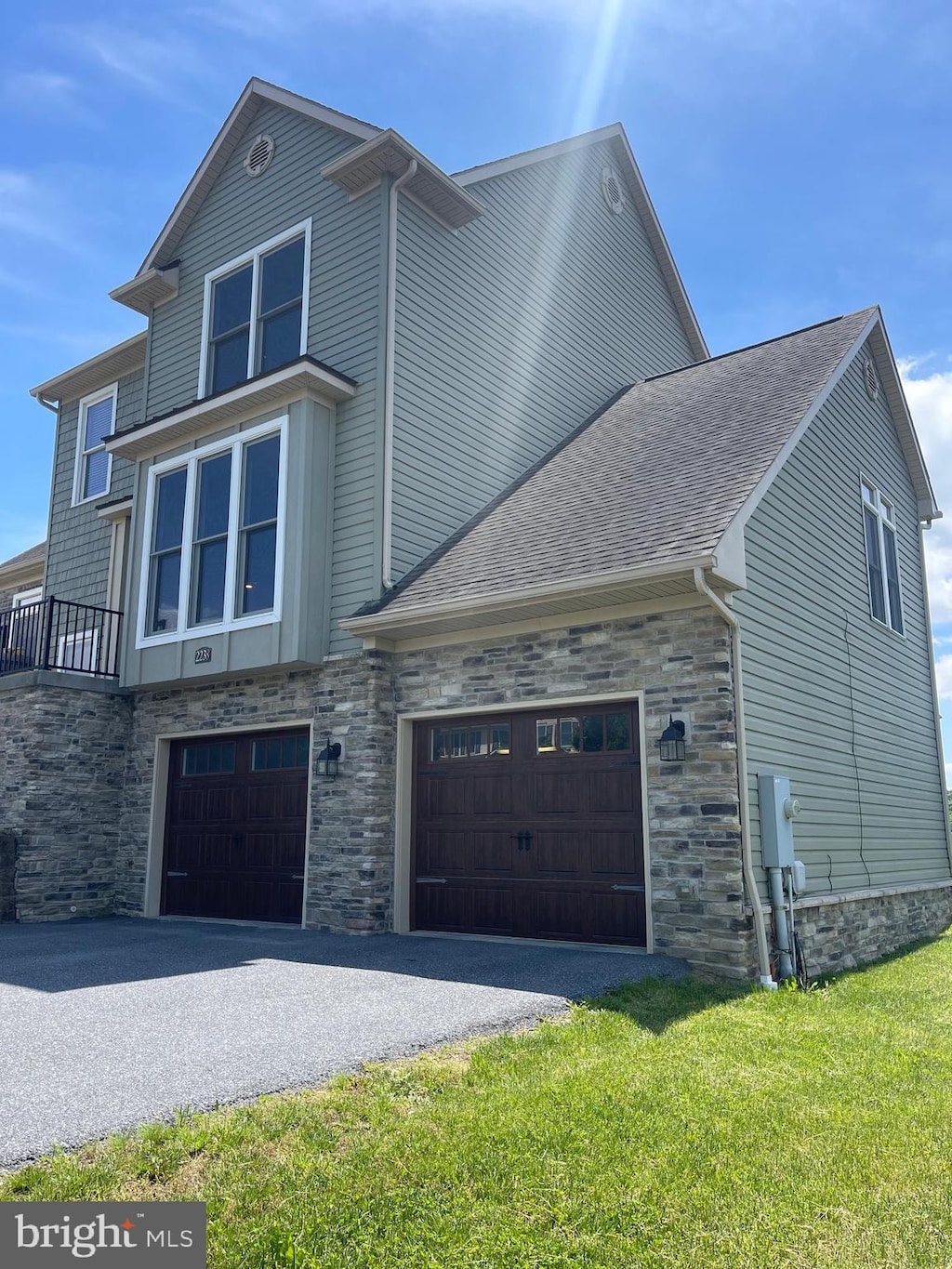 view of side of property featuring stone siding, a shingled roof, asphalt driveway, an attached garage, and a lawn