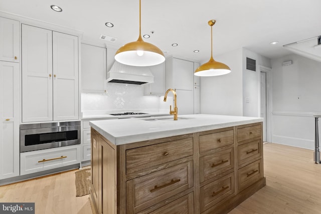 54 Wolfe St, Alexandria, VA 22314 - kitchen with a sink, light wood-type flooring, tasteful backsplash, a center island with sink, and hanging light fixtures