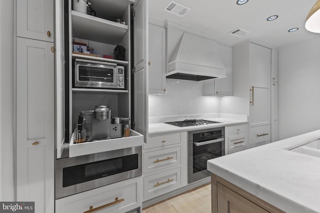 54 Wolfe St, Alexandria, VA 22314 - kitchen with stainless steel appliances, light countertops, custom exhaust hood, white cabinets, and recessed lighting