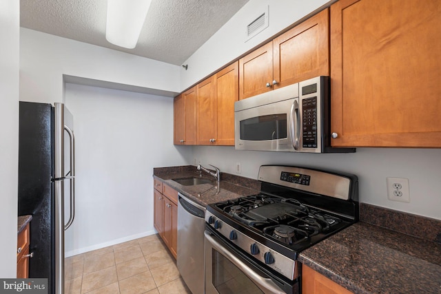 4801 Fairmont Ave Unit 804, Bethesda, MD 20814 - kitchen with stainless steel appliances, a sink, brown cabinetry, a textured ceiling, and dark stone countertops