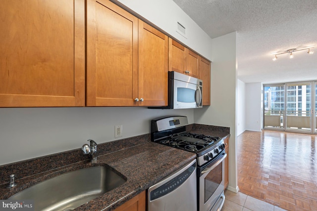 4801 Fairmont Ave Unit 804, Bethesda, MD 20814 - kitchen featuring appliances with stainless steel finishes, a sink, a textured ceiling, dark stone countertops, and brown cabinetry