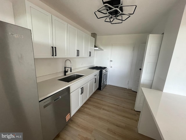 kitchen with a sink, stainless steel appliances, white cabinetry, and light wood finished floors