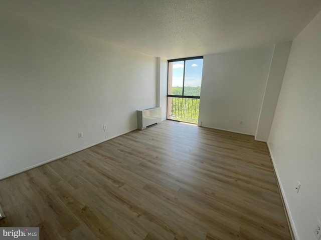 empty room with a wall of windows, wood finished floors, baseboards, and a textured ceiling