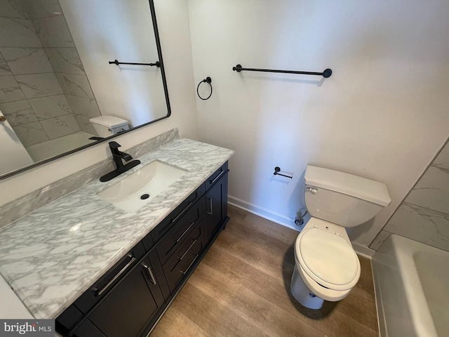full bath featuring baseboards, toilet, wood finished floors, vanity, and a bath