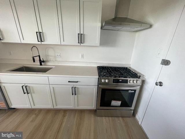 kitchen featuring stainless steel gas range, wall chimney exhaust hood, a sink, and light wood-type flooring