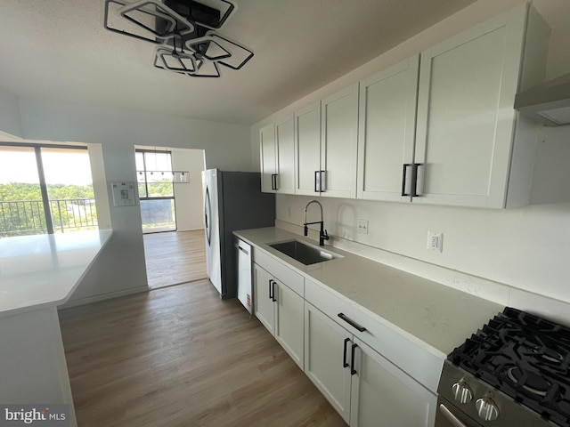 kitchen with a sink, appliances with stainless steel finishes, white cabinetry, and light wood-style flooring