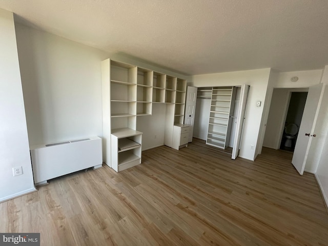 unfurnished bedroom with radiator, wood finished floors, a closet, baseboards, and a textured ceiling