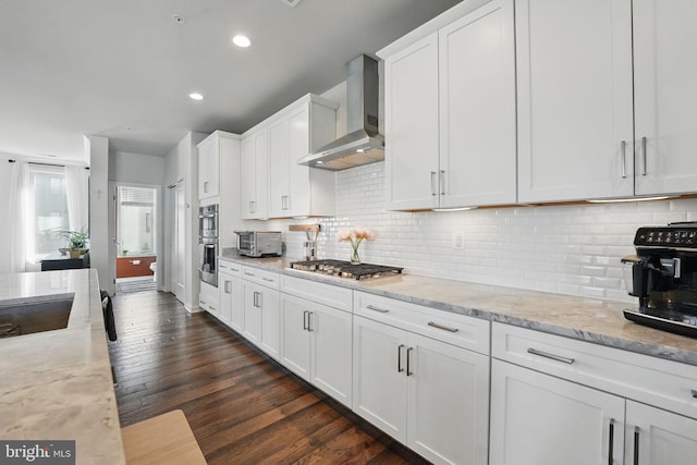 kitchen featuring wall chimney range hood, stainless steel appliances, white cabinetry, dark wood-style flooring, and light stone countertops