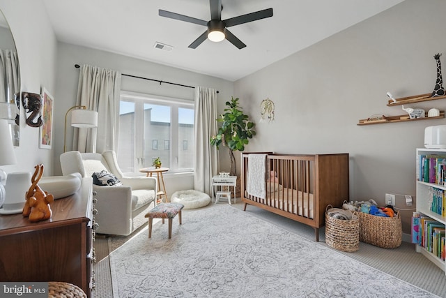 carpeted bedroom featuring a nursery area and ceiling fan