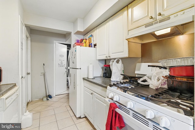 kitchen with white appliances, under cabinet range hood, light tile patterned floors, dark countertops, and white cabinets