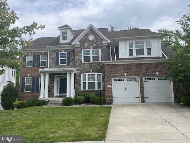 colonial-style house with a front yard, an attached garage, concrete driveway, and stone siding