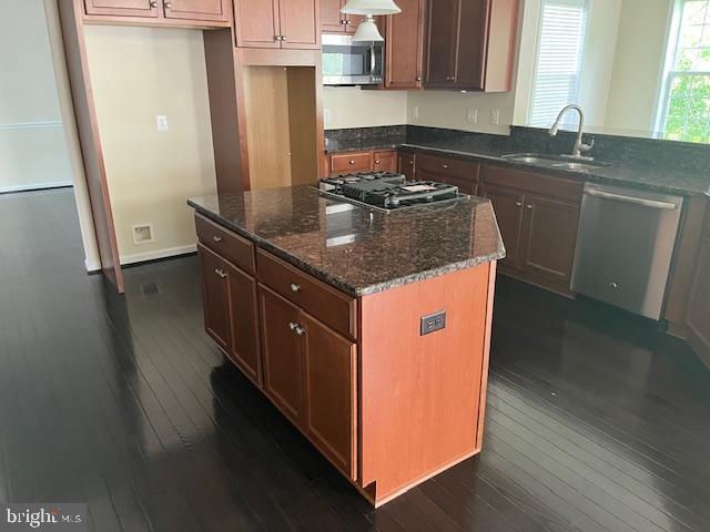 kitchen with stainless steel appliances, a sink, dark wood finished floors, dark stone countertops, and a center island