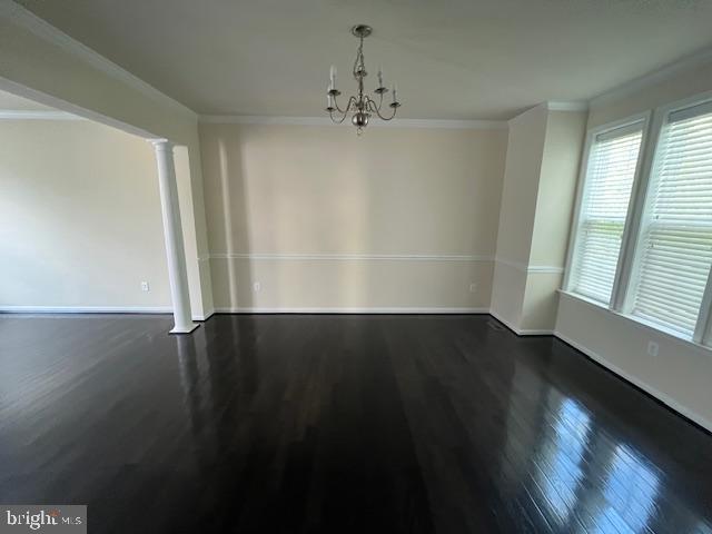 unfurnished dining area with wood finished floors, crown molding, baseboards, a chandelier, and ornate columns