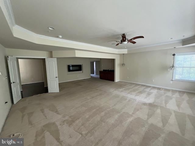 unfurnished living room featuring a tray ceiling, light carpet, ceiling fan, baseboards, and ornamental molding