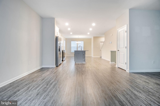 unfurnished living room featuring a chandelier, dark wood finished floors, baseboards, and recessed lighting