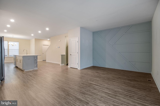 unfurnished living room featuring a sink, a chandelier, wood finished floors, a decorative wall, and baseboards
