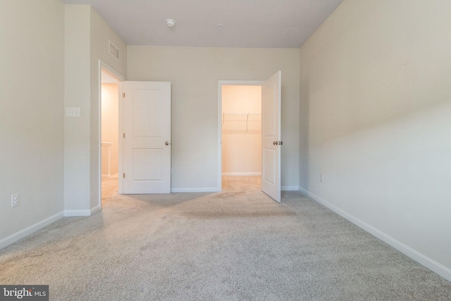 unfurnished bedroom with a walk in closet, carpet, baseboards, and a closet