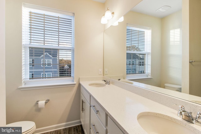 bathroom featuring toilet, healthy amount of natural light, baseboards, and double vanity