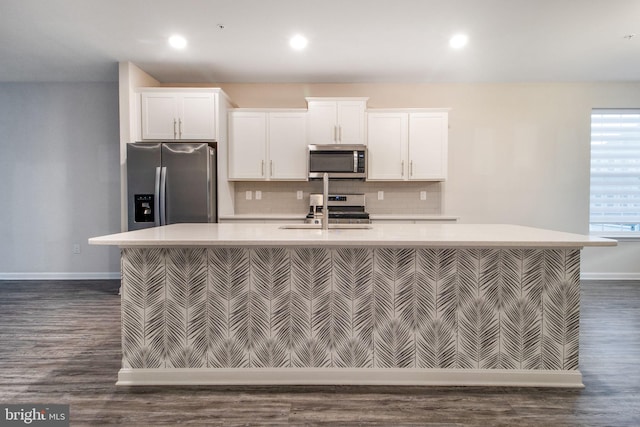 kitchen with appliances with stainless steel finishes, a sink, baseboards, light countertops, and an island with sink
