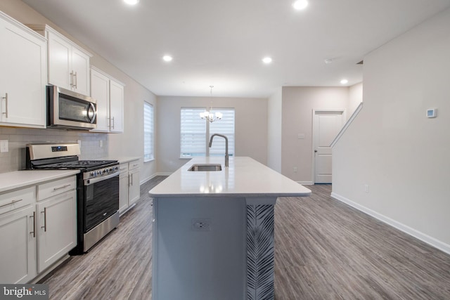 kitchen with appliances with stainless steel finishes, a sink, wood finished floors, baseboards, and a kitchen island with sink